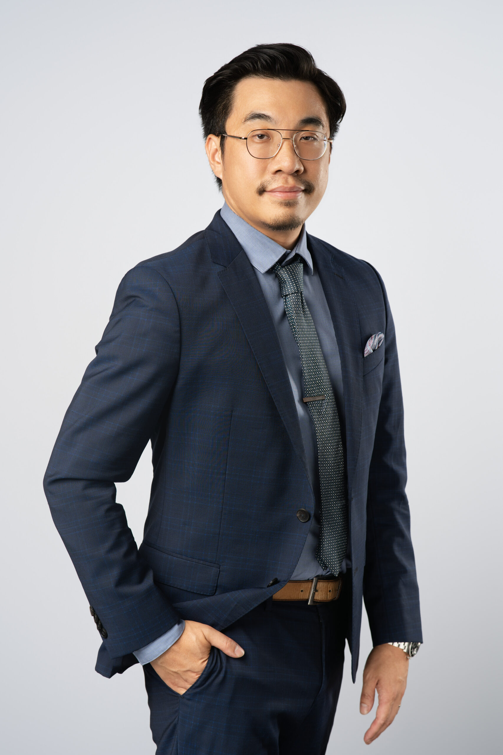 Professional headshot of Benjamin Fong, VP of Financial Reporting, standing with right hand in pocket and thumb sticking out against a grey background