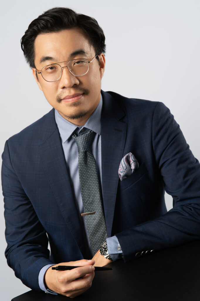 Professional headshot of Benjamin Fong, VP of Financial Reporting siting with pen in hand on black table