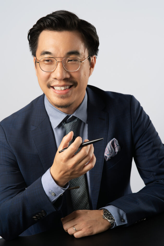 Professional headshot of Benjamin Fong, VP of Financial Reporting, sitting down with pen in hand and smiling