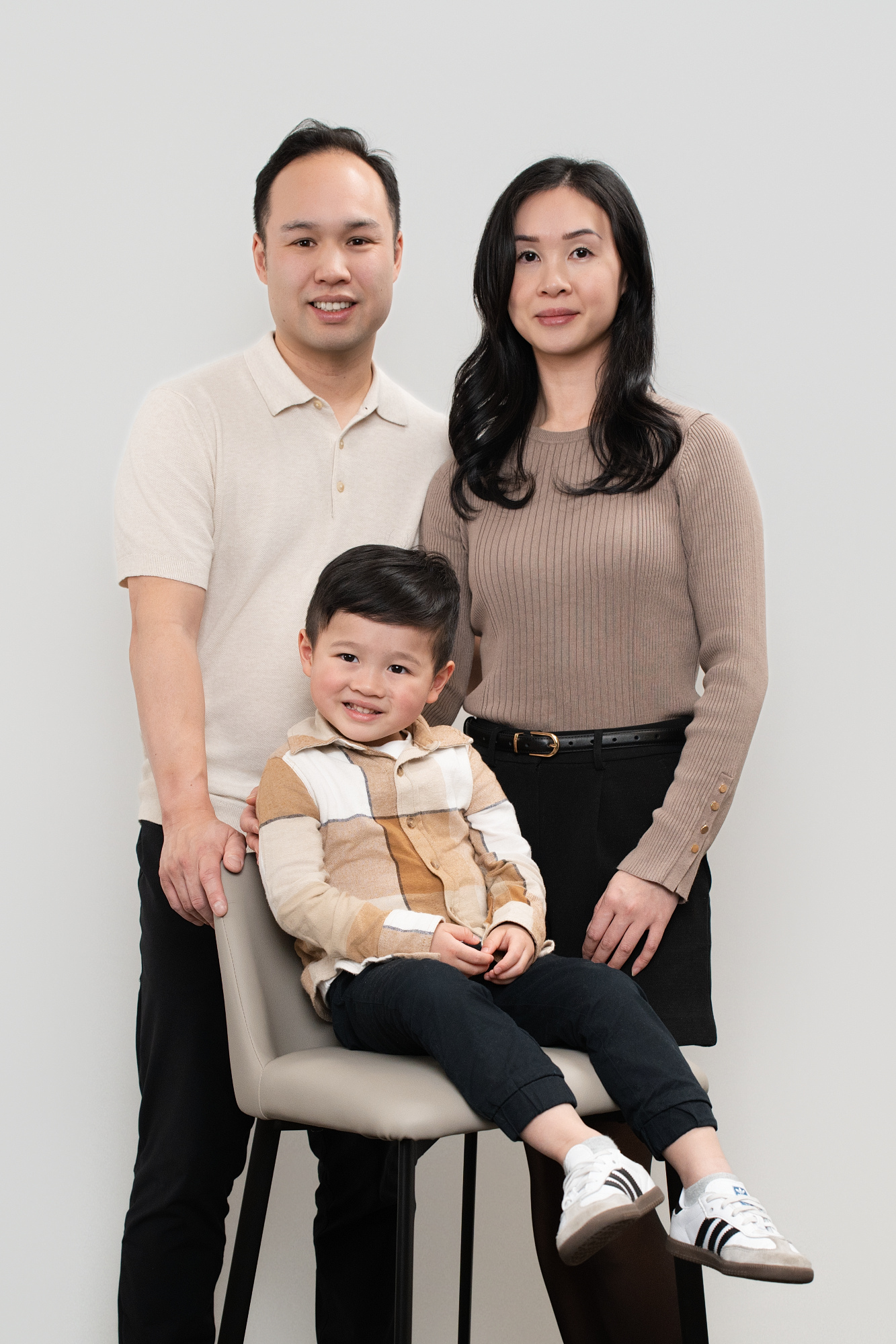 Family portrait of a father and mother standing behind their son sitting on a chair