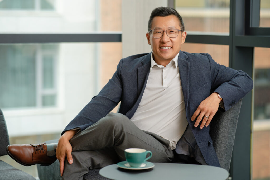 Personal branding shot of Chris Ho sitting on couch with left leg crossed over his right leg