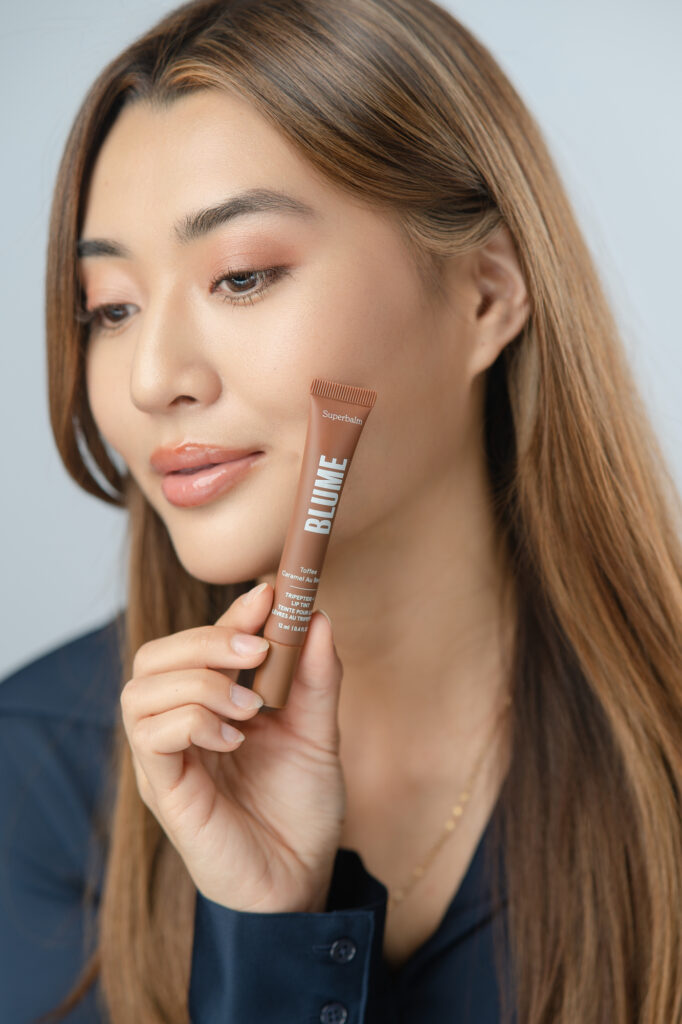 Commercial product shot of Flora Law holding Blume lip tint towards camera while facing away