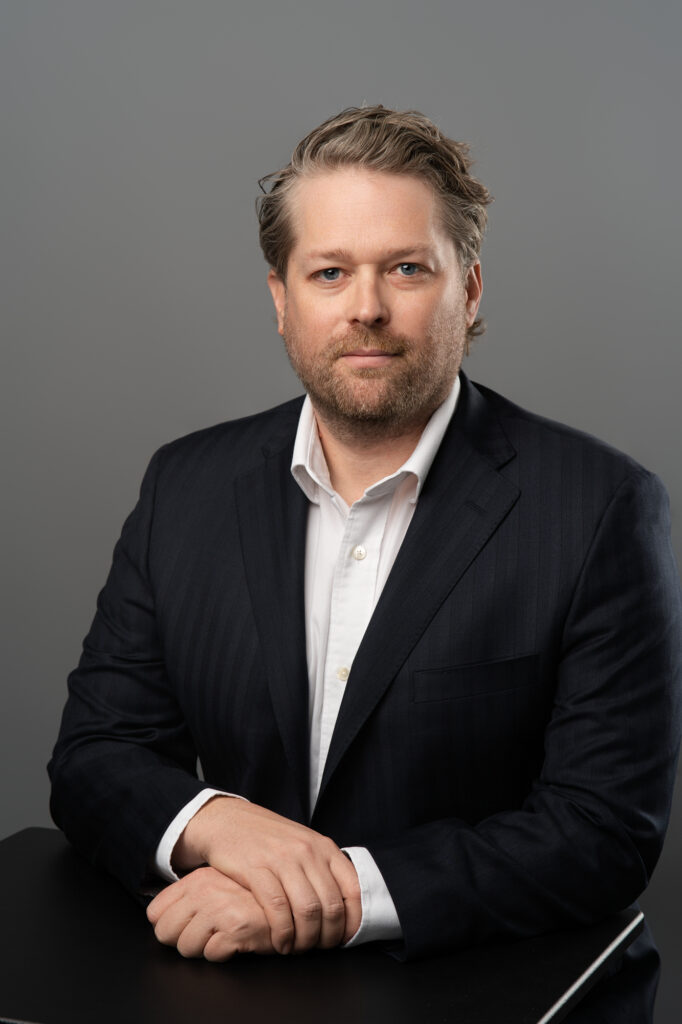 Professional man in business attire sitting down for a headshot.