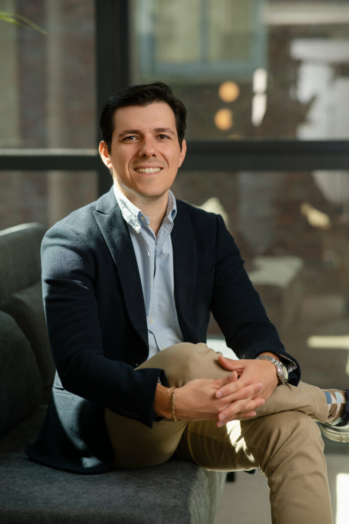 Tacio Oliveira, Global Account Manager at WeWork, professional corporate headshot sitting in a modern Vancouver office.
