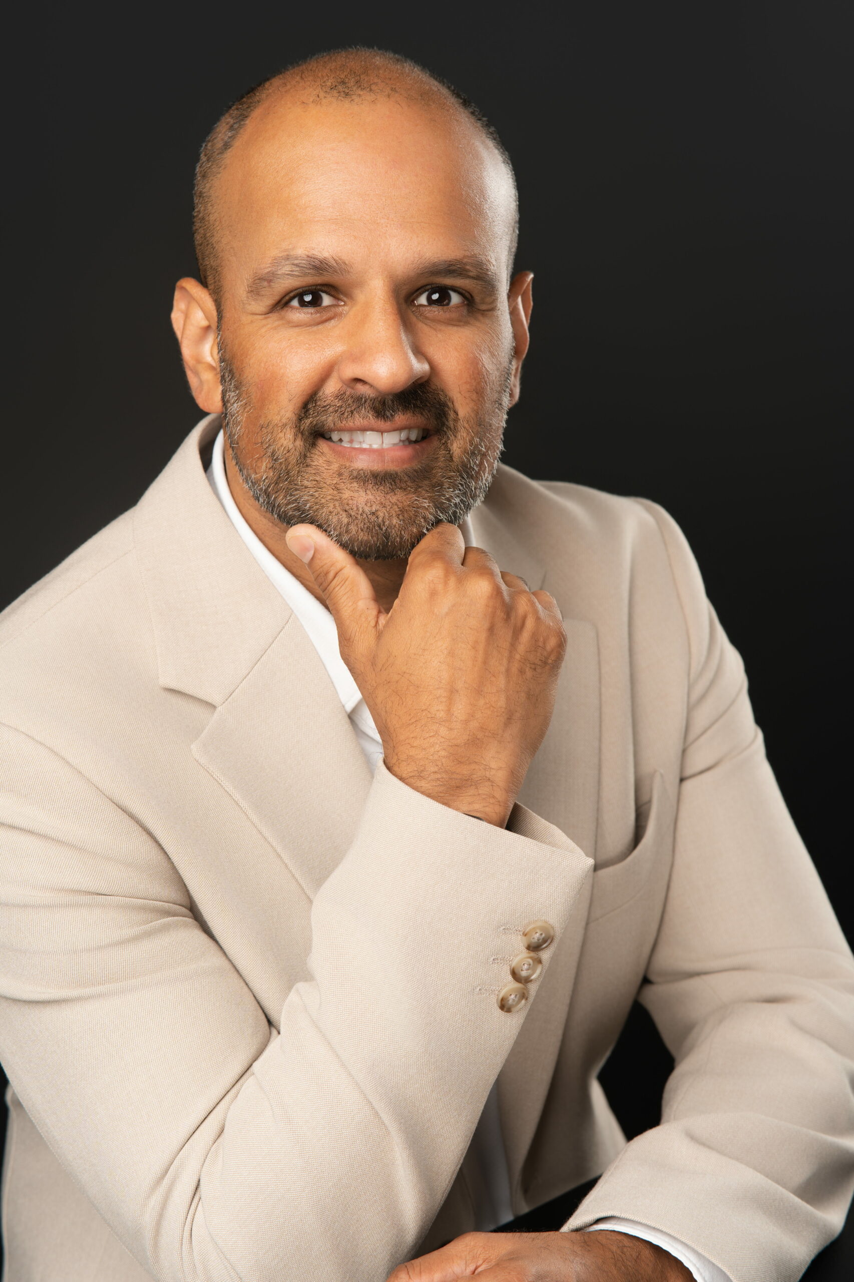 Yonel Prasad, Director of Strategic Partnership, sitting down for his corporate headshot and posed with hand on chin.